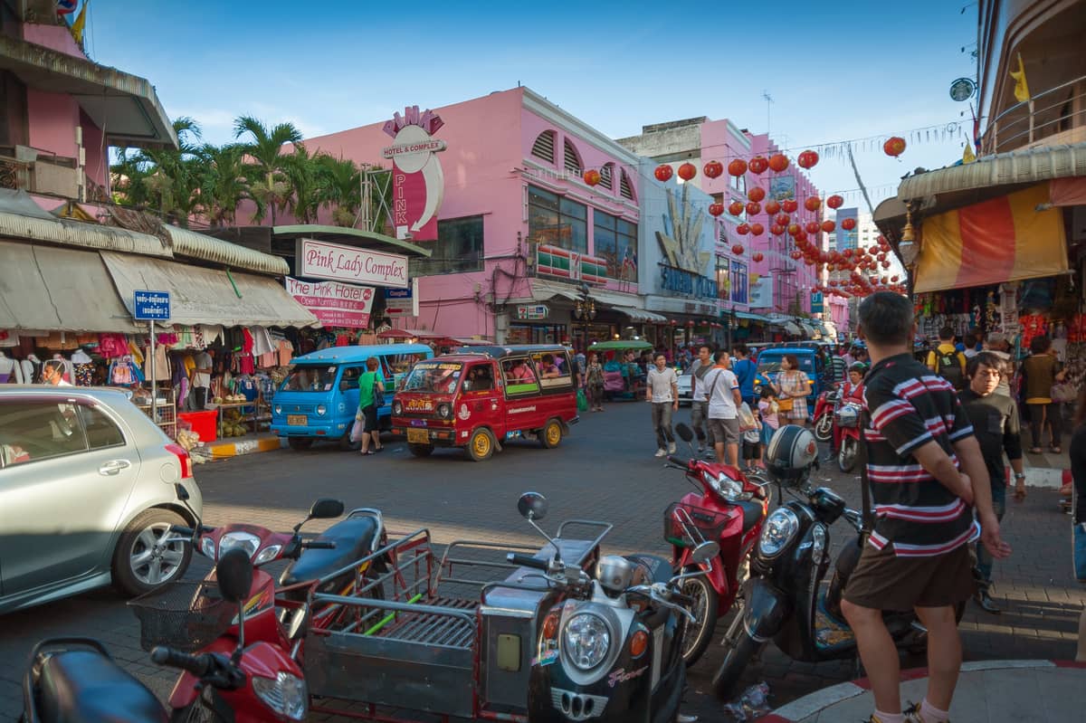 Lebhafte Straßenszene in Krabi Town mit Menschen, Motorrädern, Tuk-Tuks und bunten Ladenfront, die das tägliche Leben und die lokale Atmosphäre widerspiegelt.