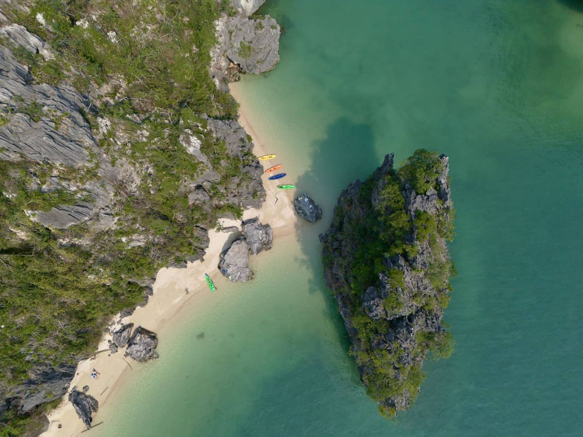 Vista aérea de kayaks en una pequeña playa de arena rodeada de aguas turquesas cristalinas y dramáticos acantilados de piedra caliza en Krabi, Tailandia.