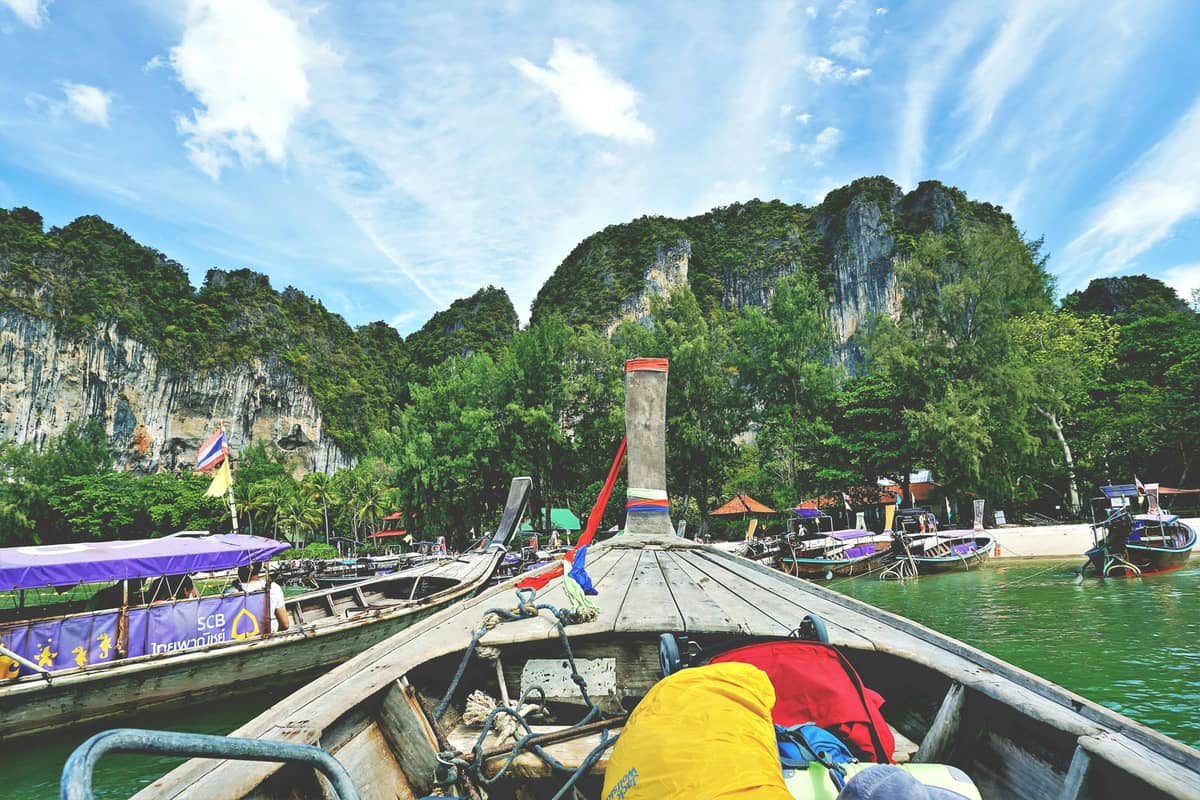 Vista desde un bote de cola larga aproximándose a la costa de Krabi, con otros botes atracados cerca de un acantilado de piedra caliza cubierto de selva.