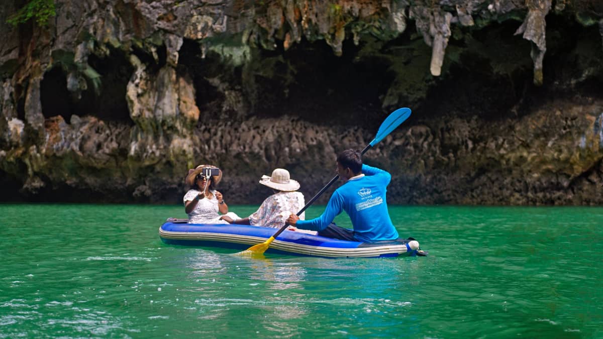 Turistas en un kayak guiado con un instructor remando en aguas verdes bajo imponentes acantilados de piedra caliza en Krabi, Tailandia.