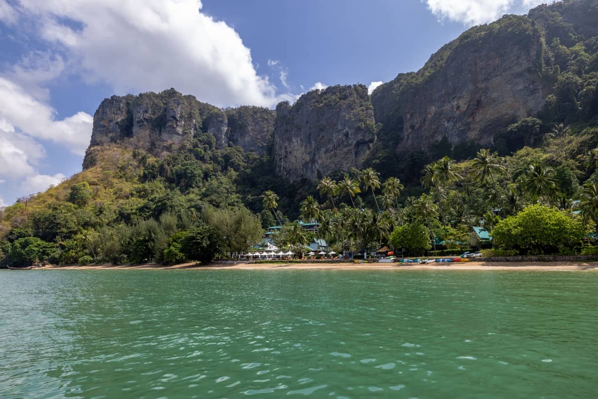 Panoramablick auf den Railay Beach in Krabi mit dramatischen Kalksteinfelsen, türkisfarbenem Wasser und Strandresorts inmitten tropischer Vegetation unter blauem Himmel.
