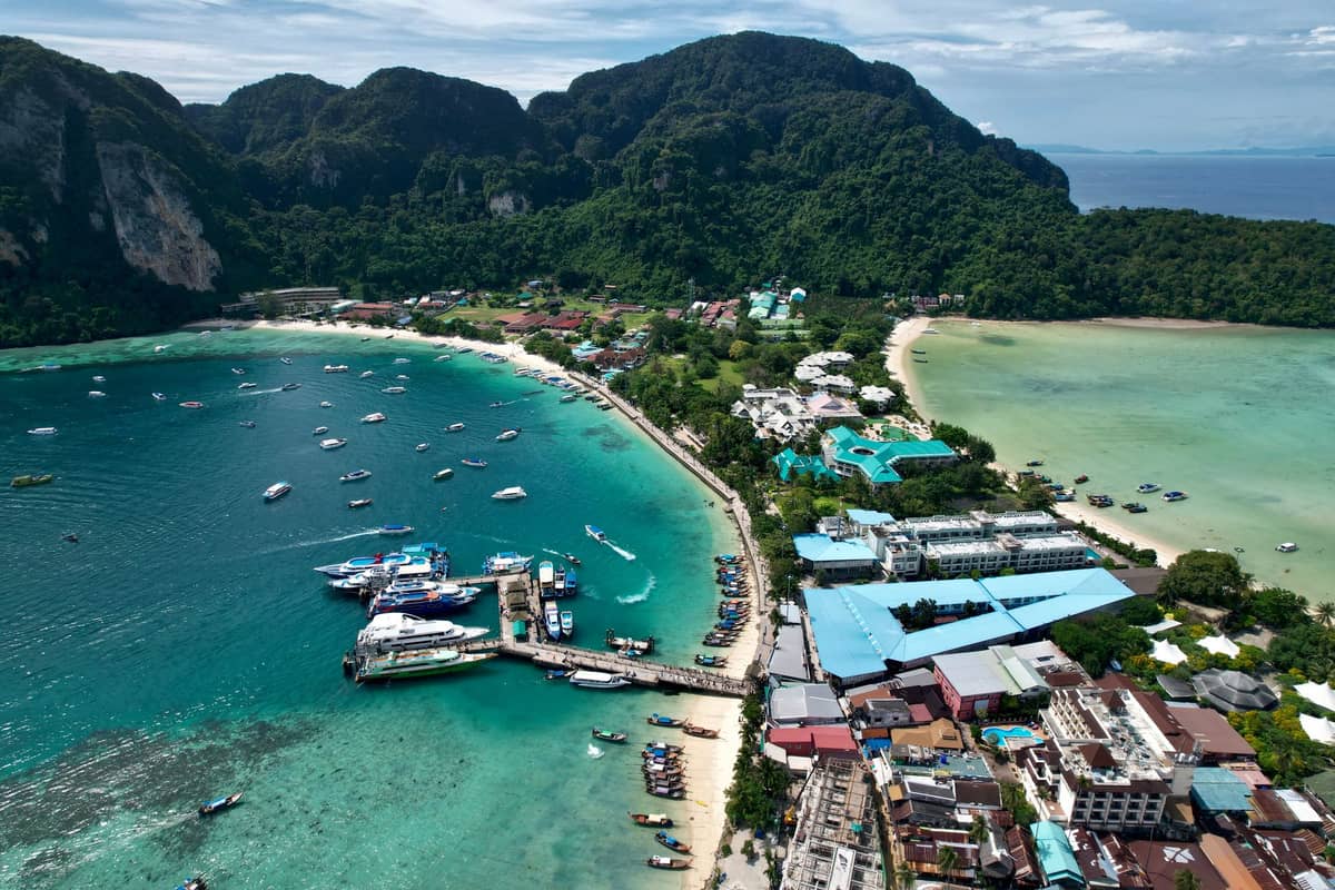 Luftaufnahme des Tonsai Pier und des Hauptdorfes auf Phi Phi Don, mit türkisfarbenem Wasser, Booten, Hotels und üppig grünen Bergen.