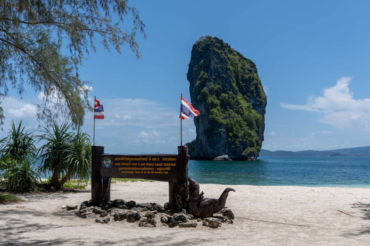 Widok krajobrazowy tropikalnej wyspy z dużymi wapiennymi krasami wyłaniającymi się z morza, piaszczystą plażą i tablicą parkową na pierwszym planie, Krabi, Tajlandia.