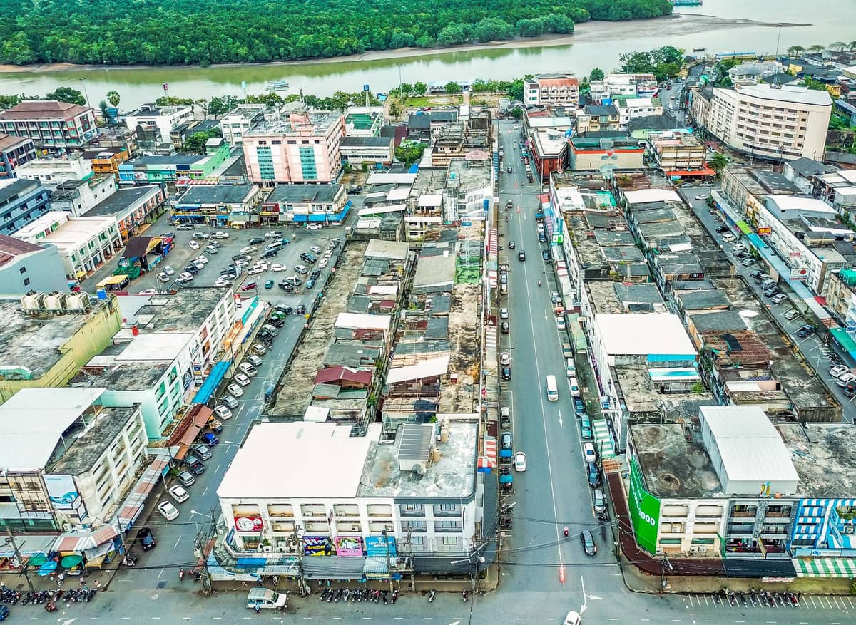 Luftaufnahme von Krabi Town mit Reihen von Shophouses und einem Fluss im Hintergrund, der die lokale städtische Umgebung zeigt.