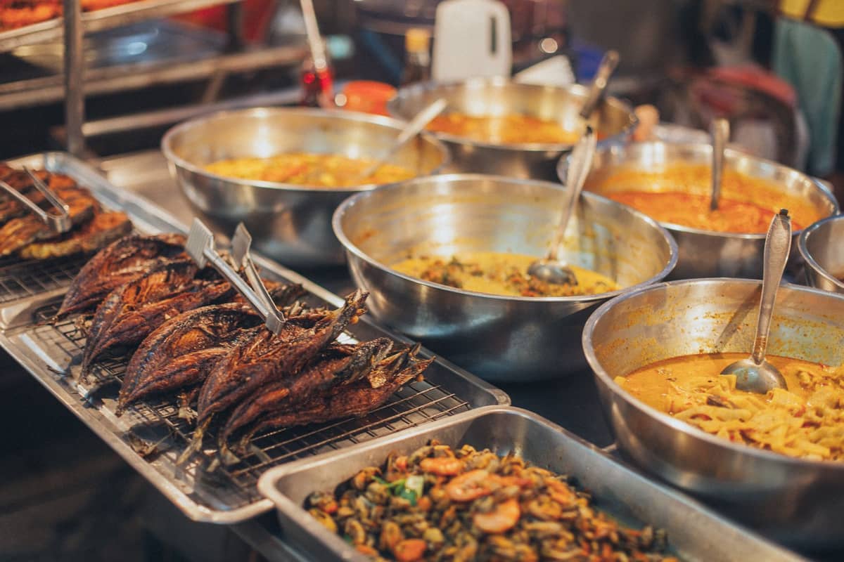 Schüsseln mit Thai-Currys, gegrilltem Fisch und gebratenen Gerichten an einem lebhaften Streetfood-Marktstand.