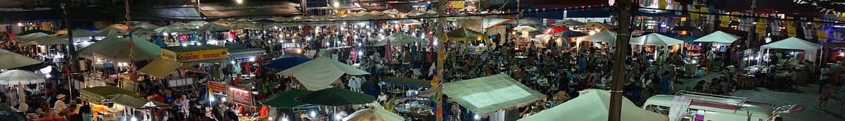 Vista notturna panoramica della Krabi Walking Street con bancarelle colorate, ombrelloni, venditori di cibo e una folla di persone che godono dell'atmosfera vivace del mercato.