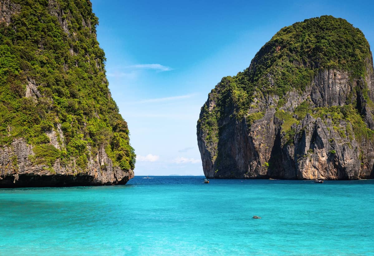 Klares türkisfarbenes Wasser und dramatische Kalksteinklippen einer Bucht der Phi Phi Islands, ohne sichtbare Menschen, unter einem sonnigen blauen Himmel.