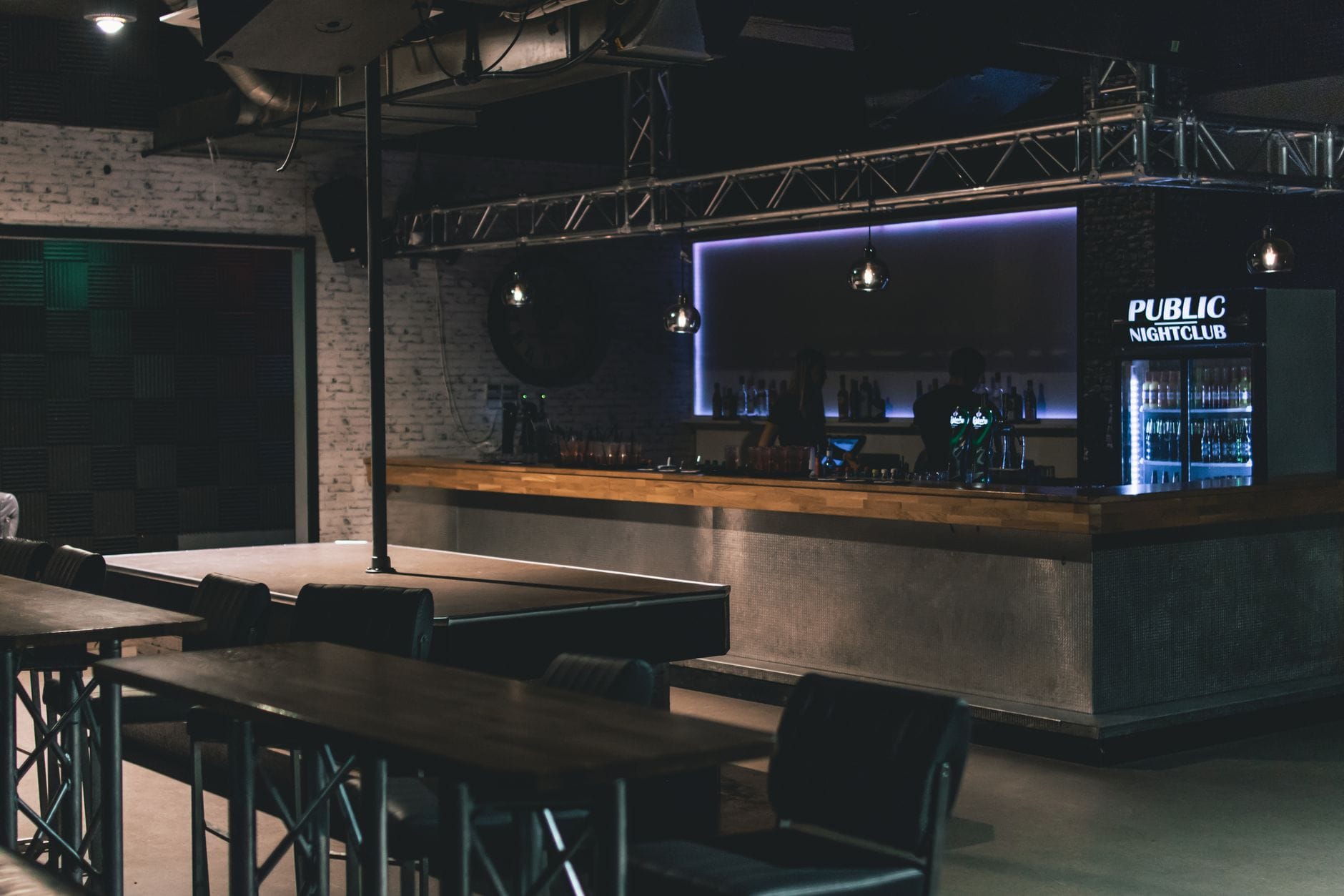 บรรยากาศไนต์คลับสมัยใหม่ มีป้ายไฟ 'PUBLIC NIGHTCLUB' ภาษาอังกฤษ เคาน์เตอร์ เครื่องดื่ม โต๊ะ เก้าอี้บาร์ ไม่มีคนพลุกพล่าน