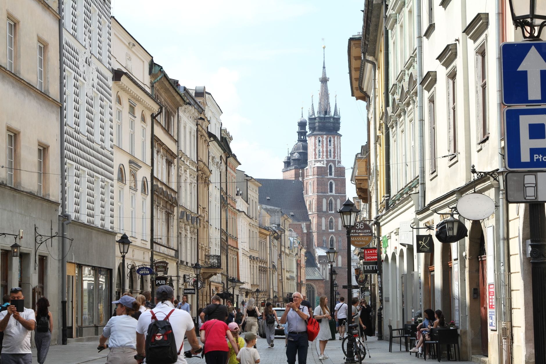 ผู้คนกำลังเดินบนถนนคนเดินในเมือง Kraków โดยมีหอคอยของมหาวิหาร St. Mary's Basilica ปรากฏให้เห็นในฉากหลัง