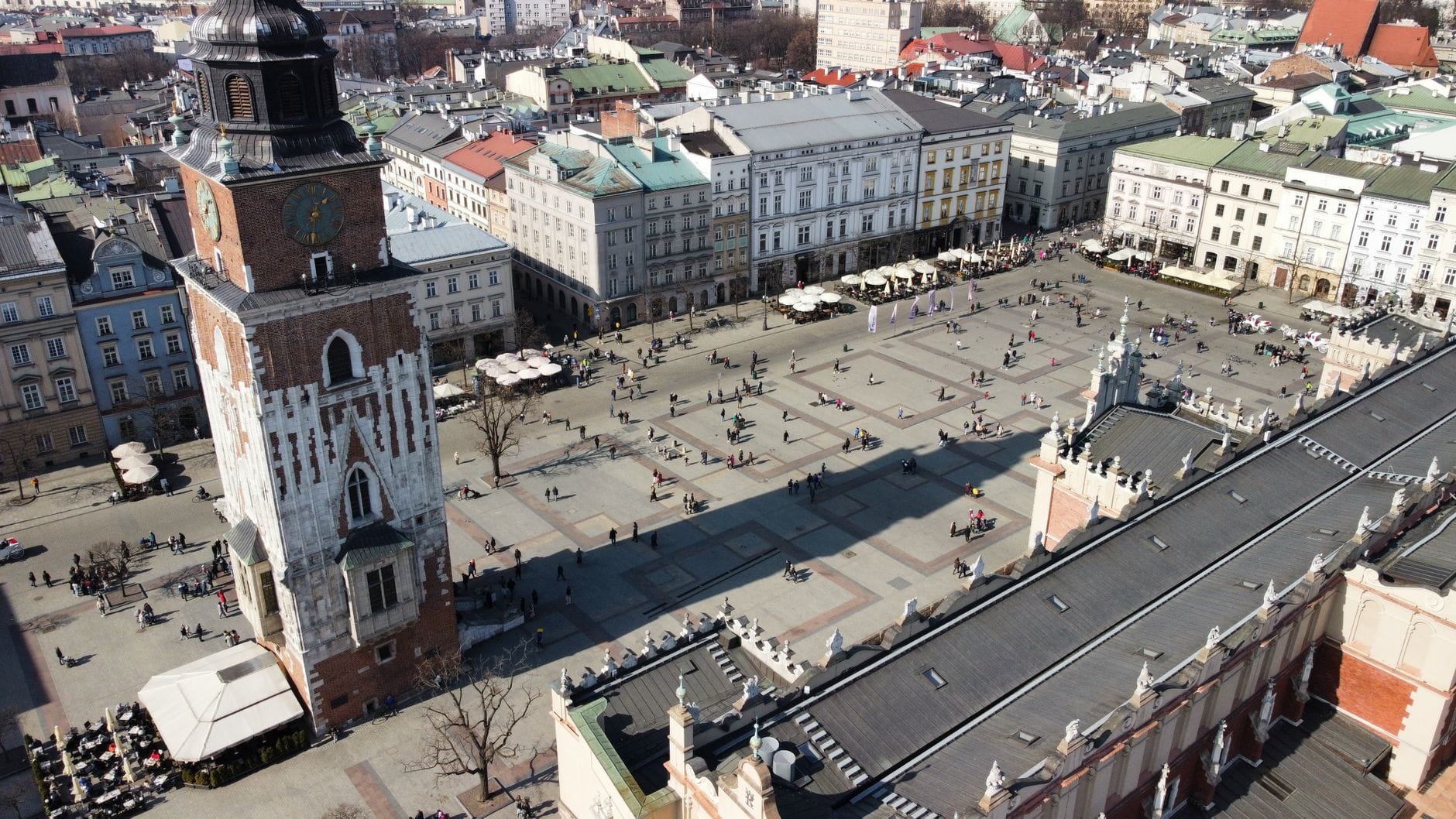 ภาพทางอากาศของจัตุรัสตลาดหลักของเมือง Kraków พร้อมอาคารประวัติศาสตร์ หอคอย และผู้คนที่เดินอยู่ในลานกว้าง