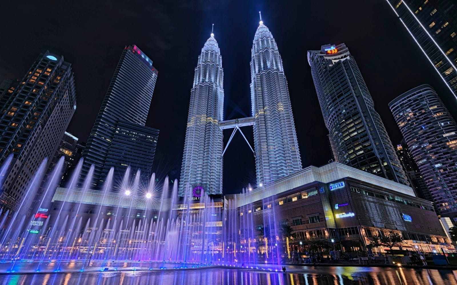 Colorful fountain lights dance beneath the sparkling Petronas Towers, capturing the vibrant nightlife around Suria KLCC shopping mall.