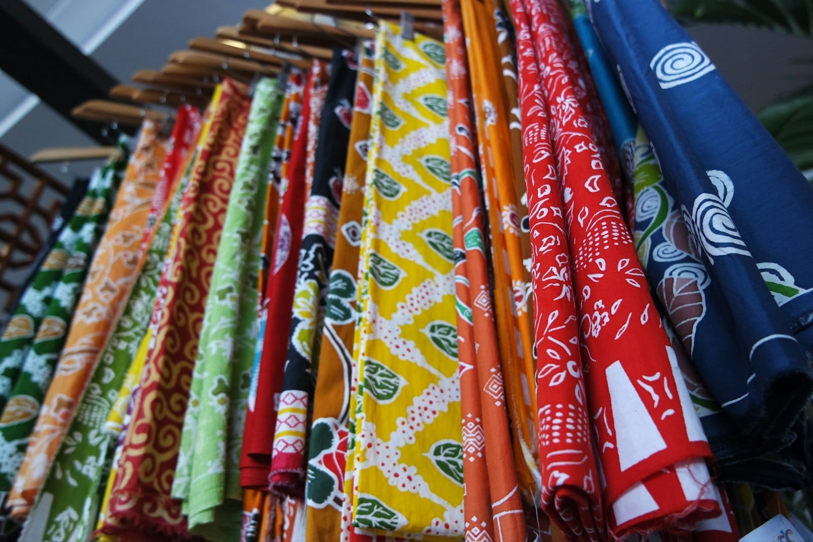Colorful Malaysian batik fabrics hanging on wooden racks inside a Kuala Lumpur shopping mall, showcasing intricate patterns and vibrant hues.