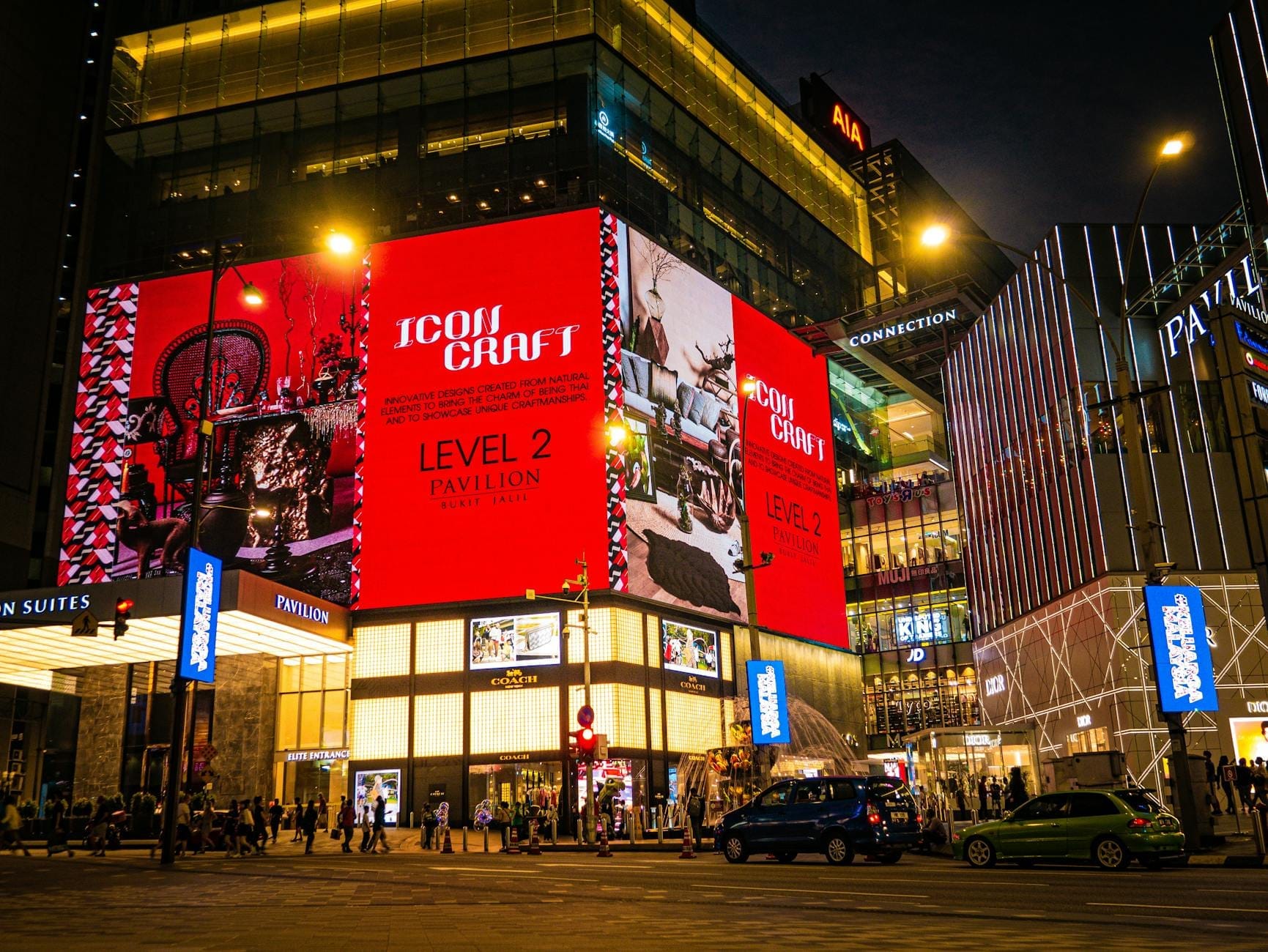 Exterior of Pavilion Kuala Lumpur shopping mall at night, featuring large illuminated digital billboards, luxury storefronts, and city street traffic.