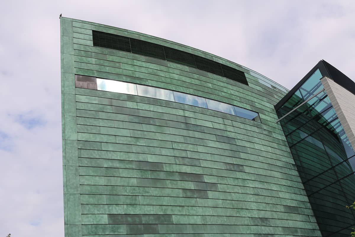 Nahaufnahme der markanten geschwungenen Fassade des Kumu Kunstimuseums aus grünem Kupfer und Glas unter einem überwiegend bewölkten Himmel.