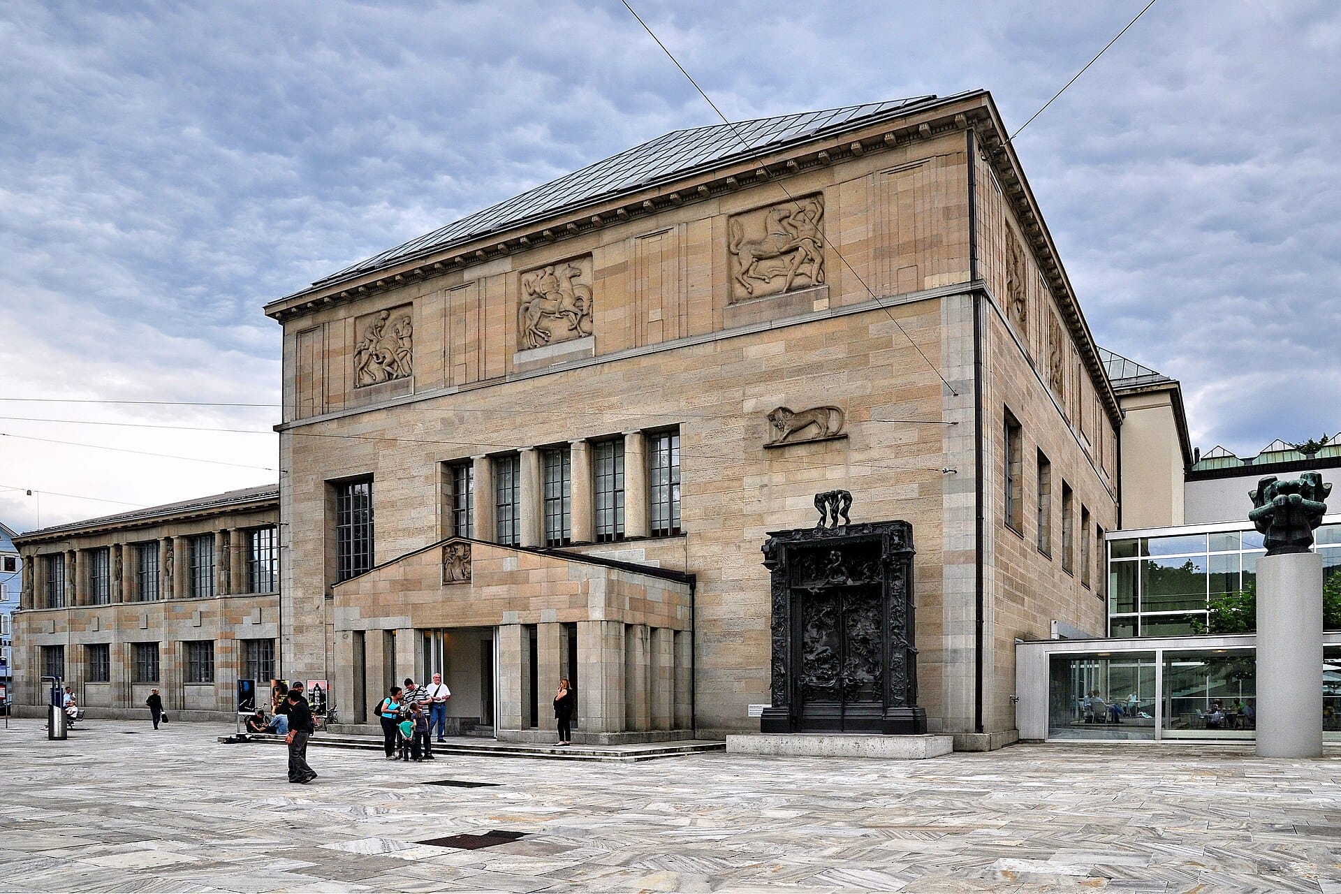 ภาพมุมกว้างด้านหน้า Kunsthaus Zürich เห็นด้านหน้าอาคารสไตล์ Beaux-Arts หน้าต่างบานใหญ่ ประติมากรรม Gates of Hell ของโรแดงและจัตุรัสหน้าพิพิธภัณฑ์