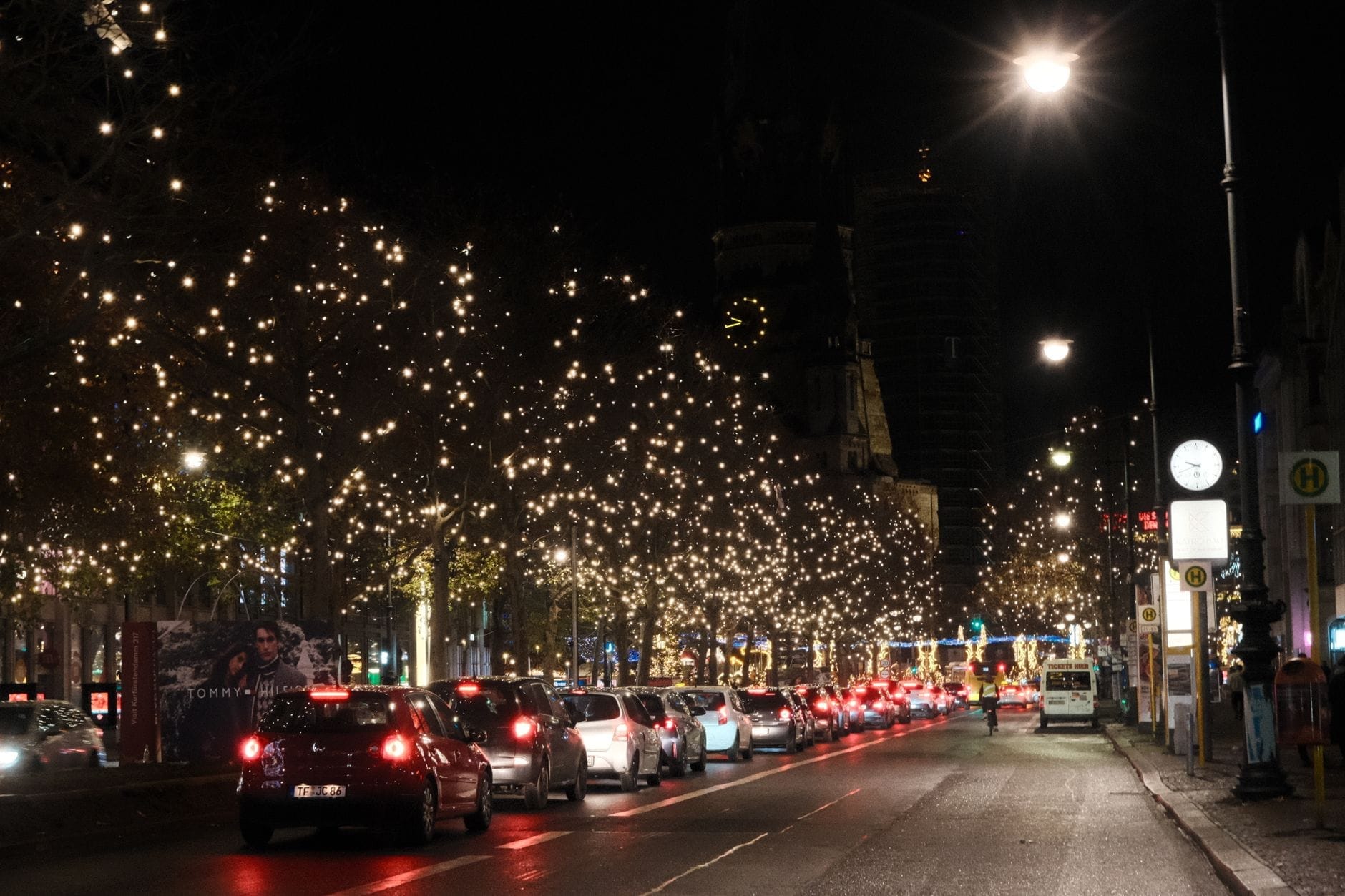 Vista notturna del Kurfürstendamm con alberi illuminati da luci scintillanti e auto lungo il grande viale, in un'atmosfera vivace e festosa tipica di Berlino.