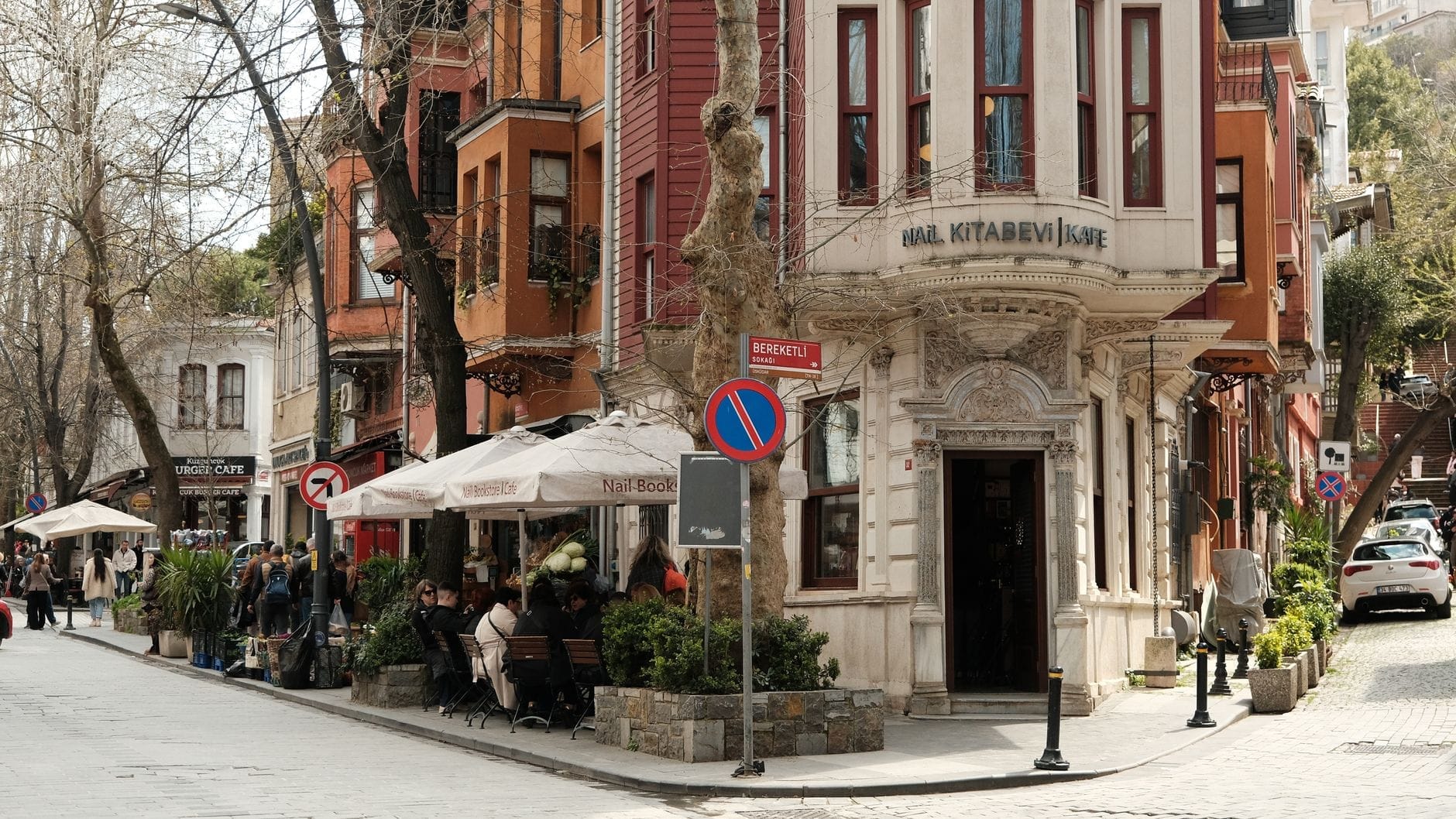 Scorcio di una strada di Kuzguncuk con case di legno dai colori pastello, tavolini all'aperto e abitanti rilassati in un'atmosfera vivace e piena di fascino.