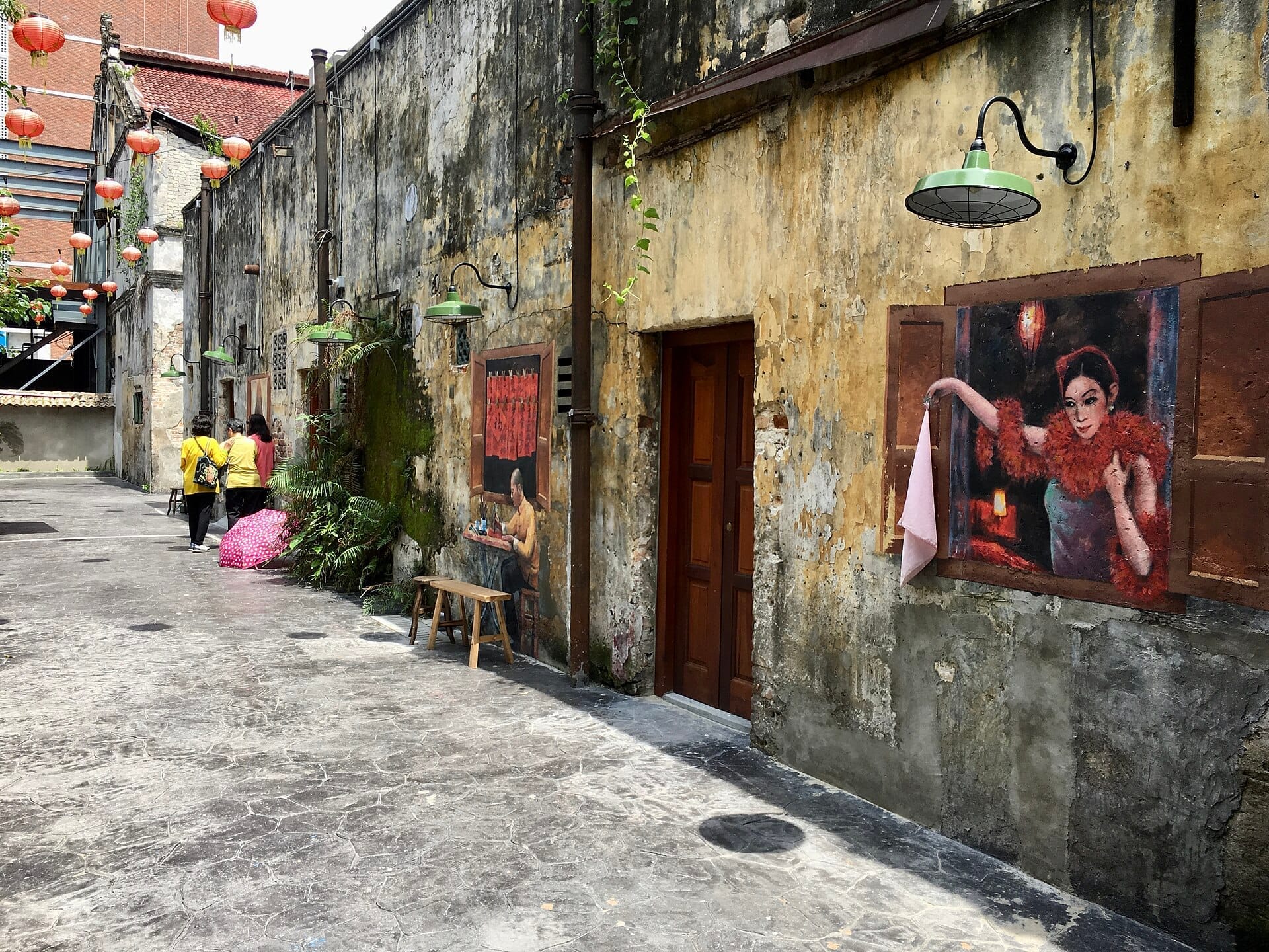 Kwai Chai Hong's weathered alleyway with colorful murals, faded yellow walls, green lamps, and red lanterns, viewed in Kuala Lumpur's Chinatown.