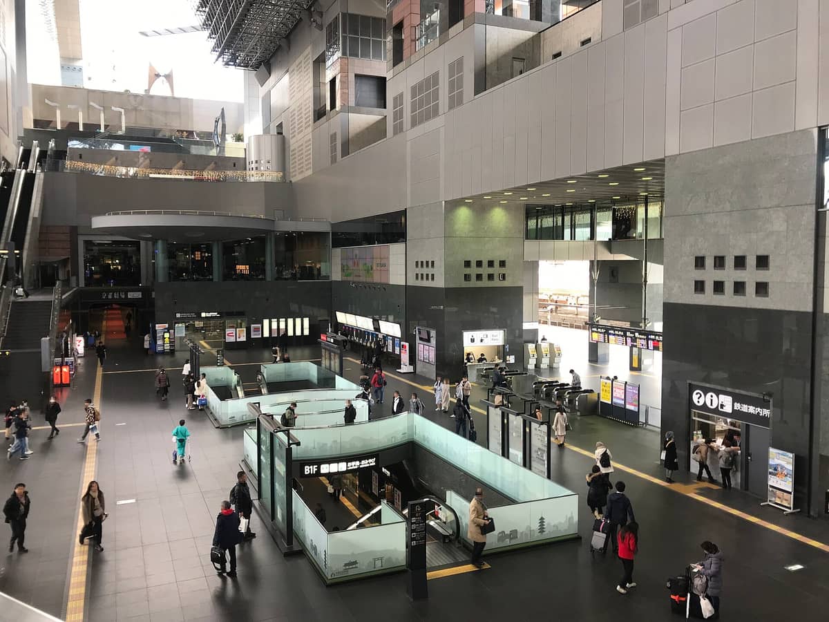 Wide view of the busy interior concourse of Kyoto Station with people, escalators, ticket gates, and modern architectural details.