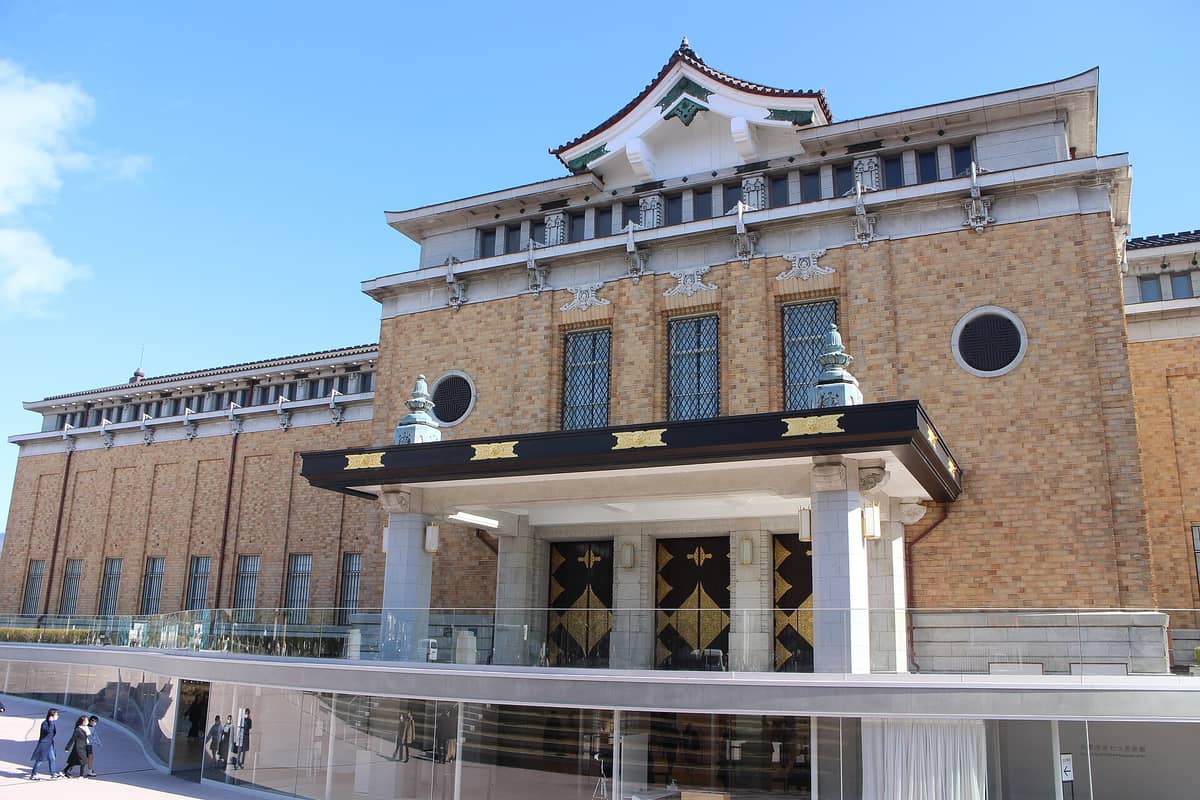 Main entrance and facade of the Kyoto City KYOCERA Museum of Art with Imperial-era architecture, golden details on the doors, and blue sky above.