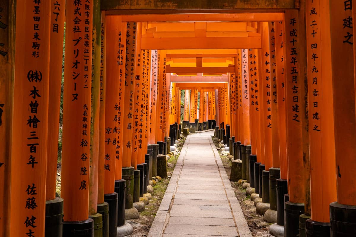 Pathway flanked by rows of bright vermillion torii gates with Japanese inscriptions at Fushimi Inari Taisha in Kyoto.