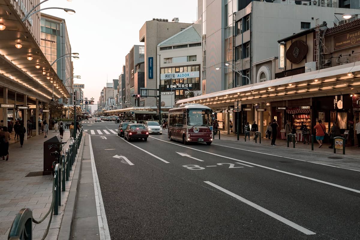 Street in Kyoto with buses, cars, and people at dusk in a busy downtown shopping area.