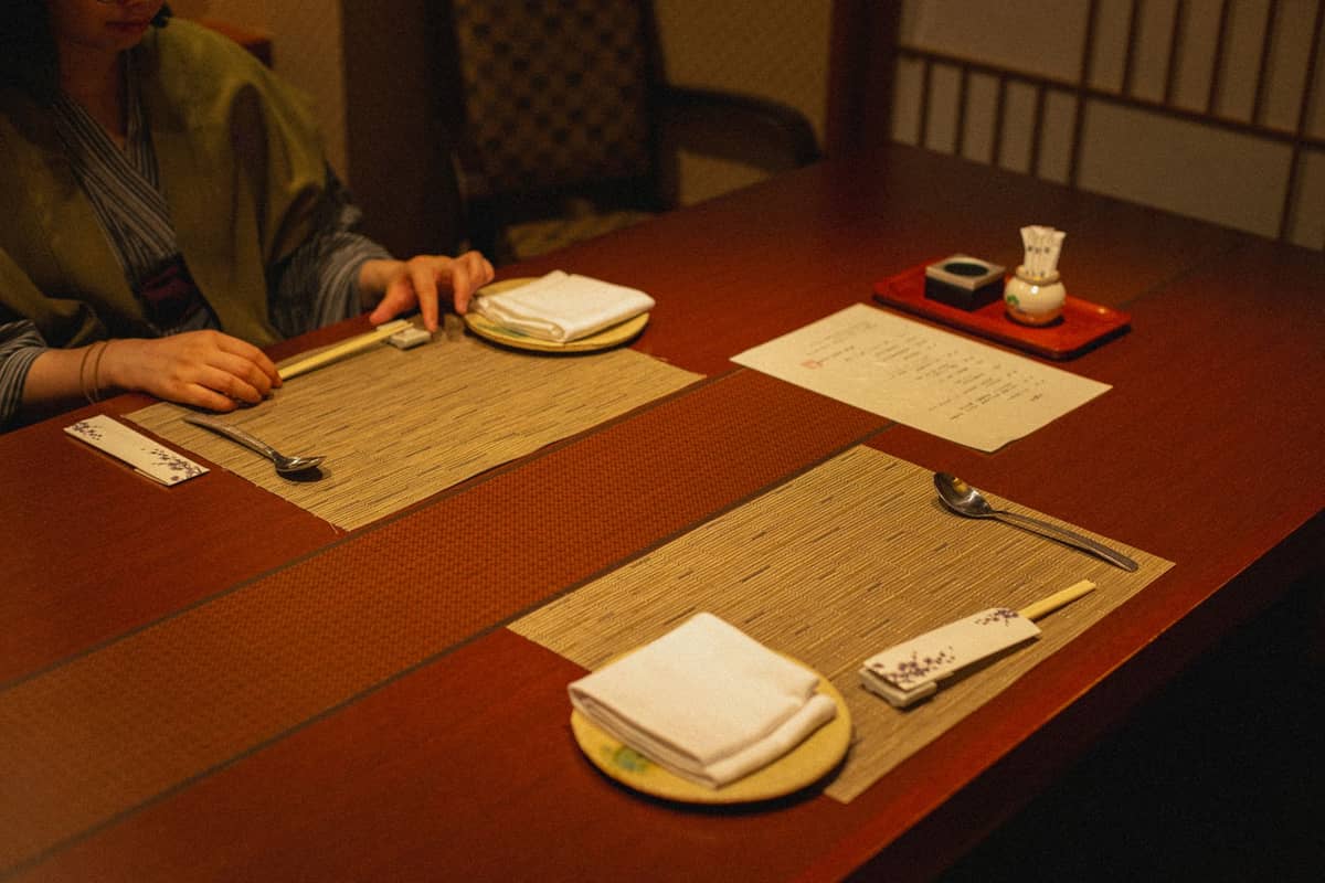 A traditional Japanese restaurant table setting with placemats, chopsticks, and menus, capturing the refined atmosphere of Kyoto dining culture.