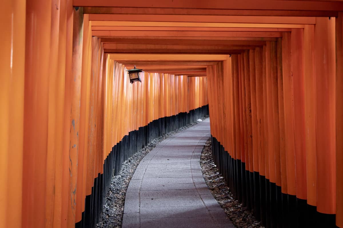 A winding pathway lined with rows of vibrant orange torii gates at Fushimi Inari Shrine in Kyoto, Japan.