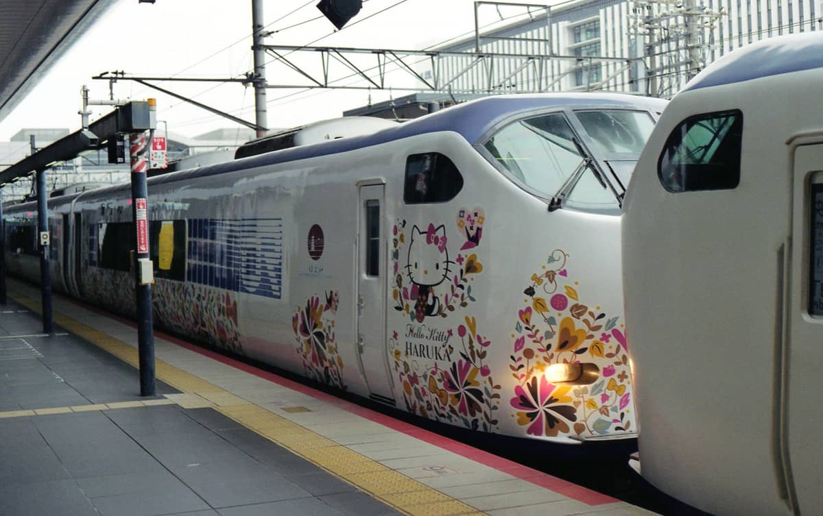 JR Haruka Limited Express train at a platform, decorated with colorful floral and Hello Kitty designs, at a Japanese railway station.