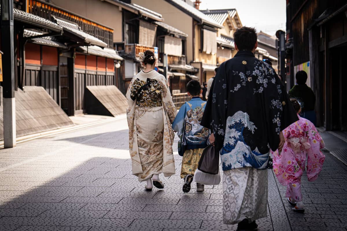 A family wearing kimono walks down a traditional Kyoto street with wooden buildings, illustrating the experience of exploring Kyoto in rented kimono.