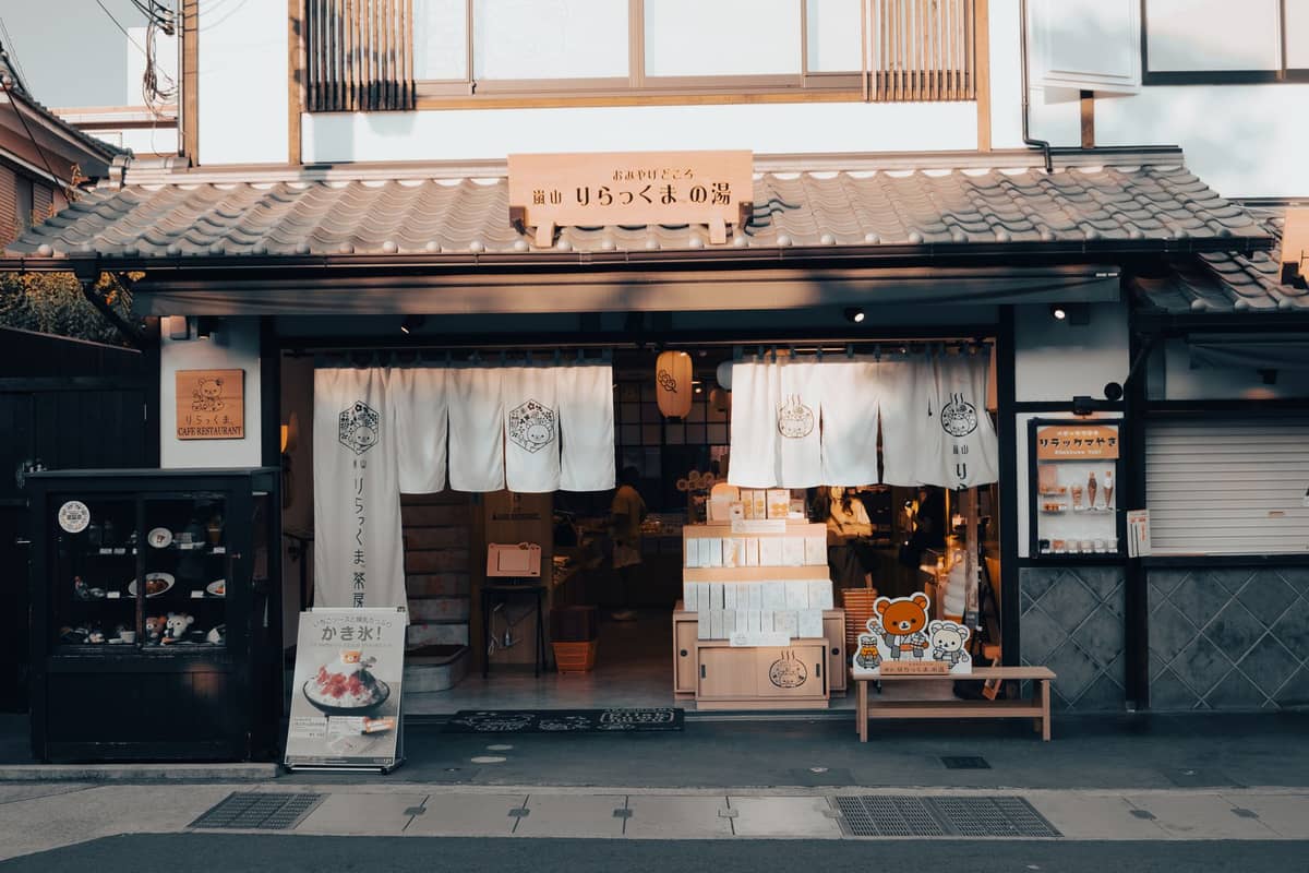 Traditional storefront in Kyoto with white noren curtains, wood signage, and shelves displaying products just inside the entrance.