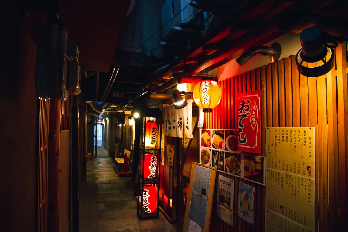Narrow lantern-lit alley in Kyoto at night lined with izakayas and bars, evoking the city’s vibrant yet intimate nightlife atmosphere.