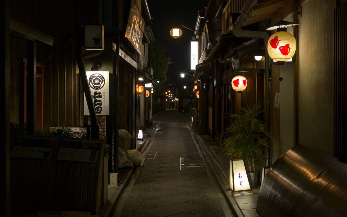 Narrow lantern-lit alley at night with wooden buildings and signs, typical of Kyoto’s Pontocho nightlife district.