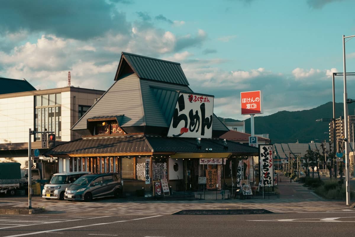 A standalone ramen shop in Kyoto with a prominent sign reading 'ramen' in Japanese, viewed from across a quiet intersection at dusk.