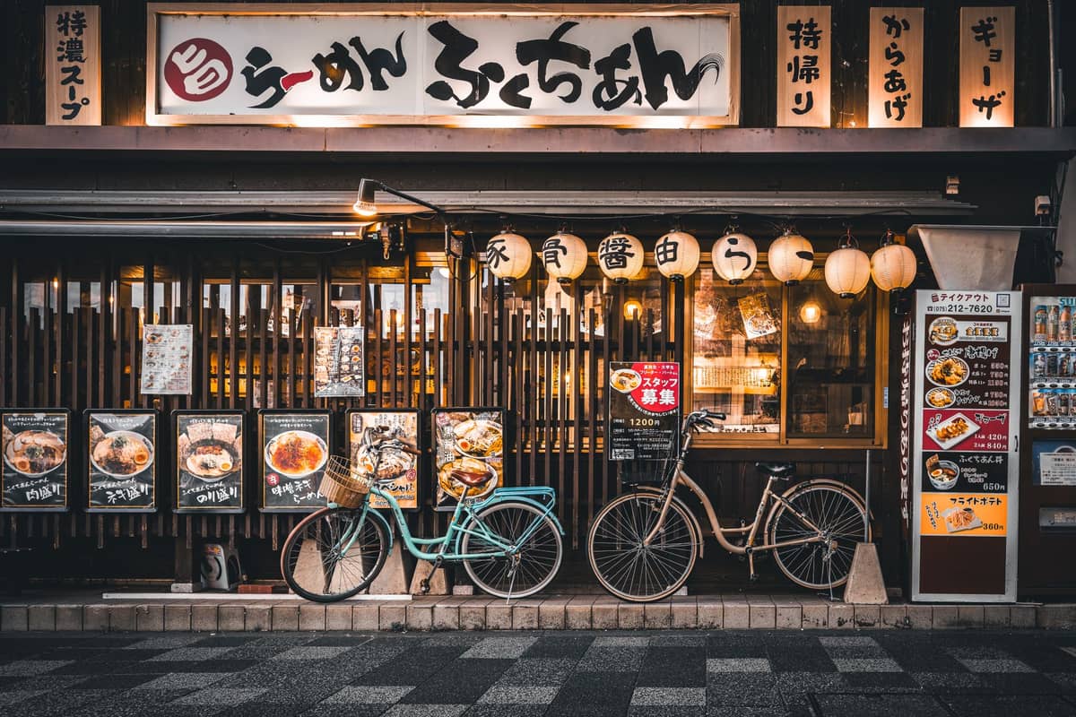 Warmly lit ramen shop exterior in Kyoto with Japanese signage, paper lanterns, and two bicycles parked outside the entrance.
