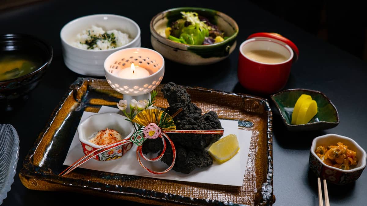A beautifully arranged Japanese kaiseki meal with multiple small dishes, rice, soup, vegetables, and decorative plating on a black table.