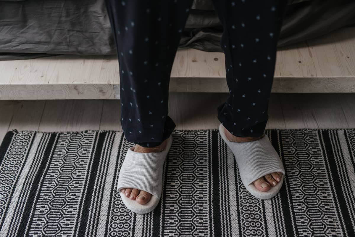 Close-up of feet in white slippers standing on a patterned rug, suggesting indoor footwear etiquette.