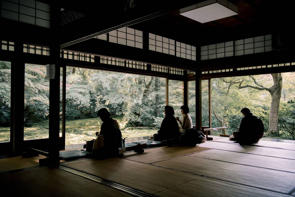 Tatami room with people sitting beside open shoji doors, overlooking a lush Japanese garden in daylight