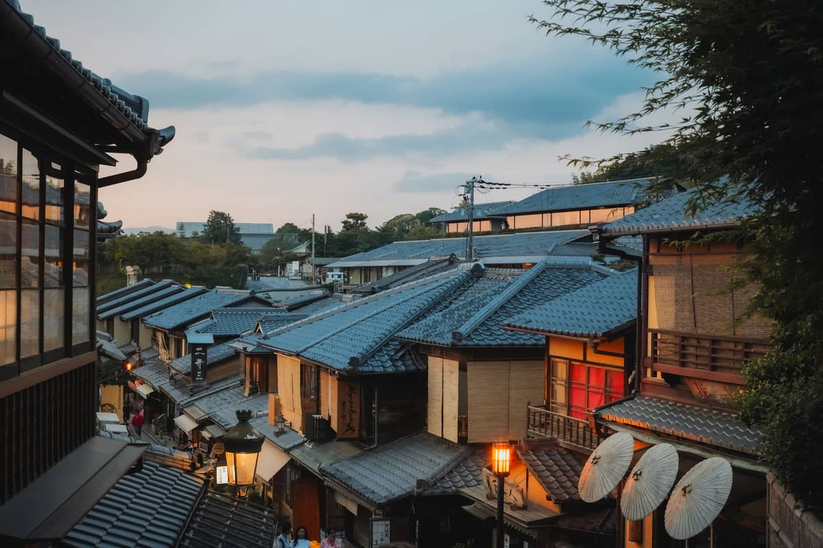 Traditional wooden machiya rooftops and lantern-lit street in a historic Kyoto district at dusk, evoking the atmosphere around Kyoto ryokans.