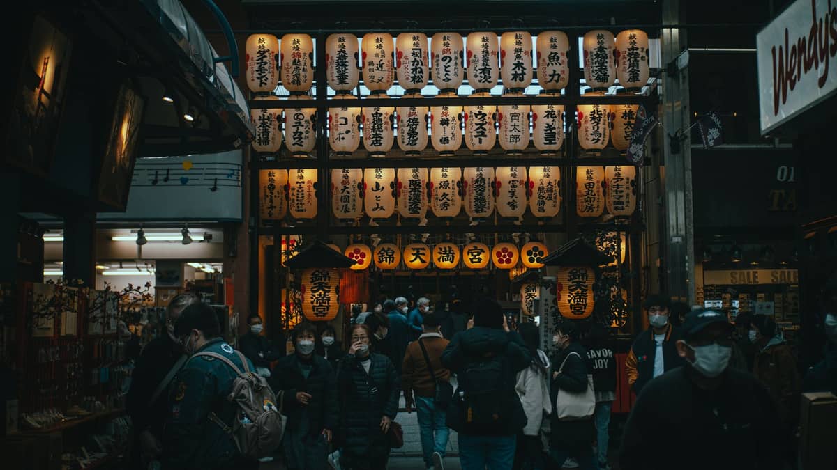 Crowded entrance to Nishiki Market in Kyoto, decorated with rows of illuminated Japanese lanterns and bustling with shoppers.