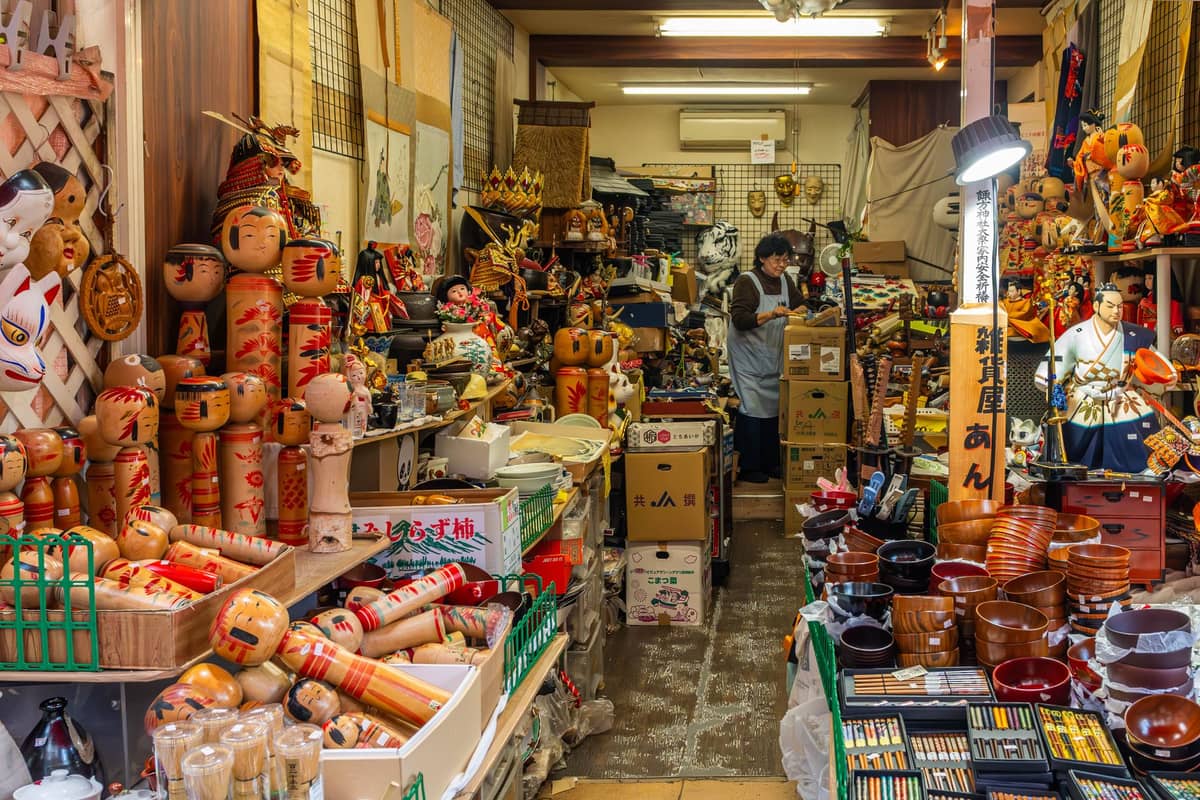 Packed Kyoto craft and souvenir shop with shelves full of wooden dolls, lacquerware, chopsticks, toys, and traditional Japanese crafts.