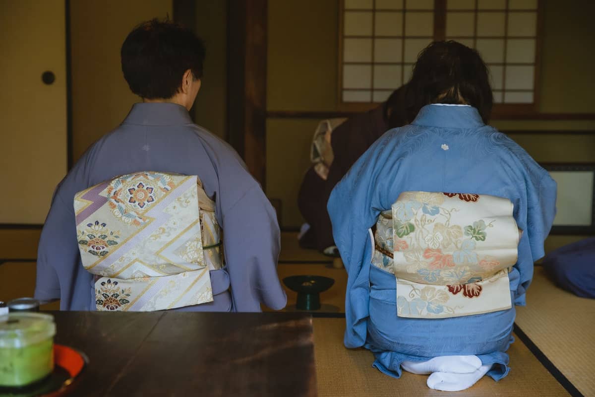 Women in kimono seated quietly on tatami in a traditional Japanese tea room, highlighting the atmosphere of respect and tranquility.