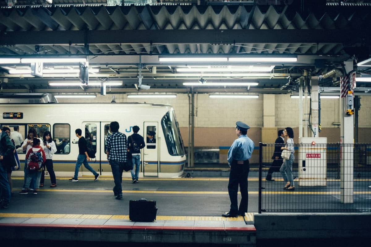 Commuters and a security guard on a busy JR platform with a white train, typical scene for Kyoto-Nara day trips.