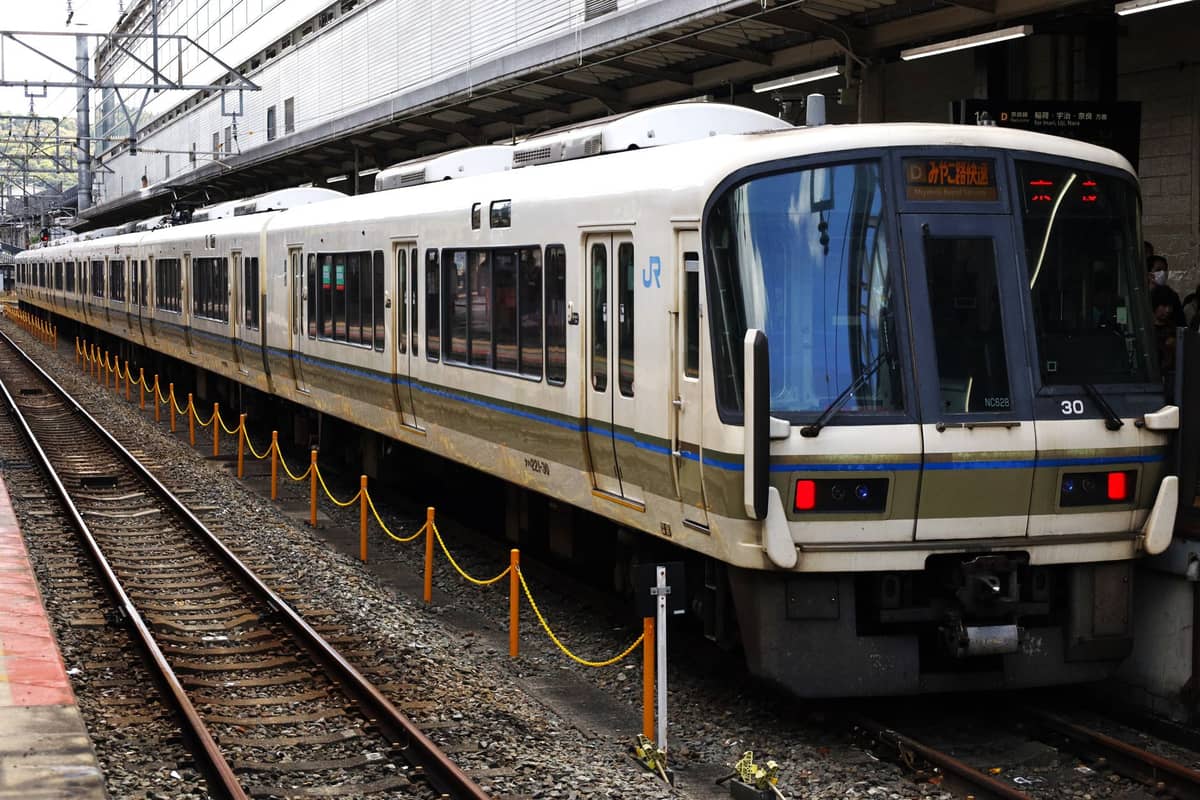 Platform view of a JR train stopped at a Japanese railway station, with platform and tracks visible in daylight.