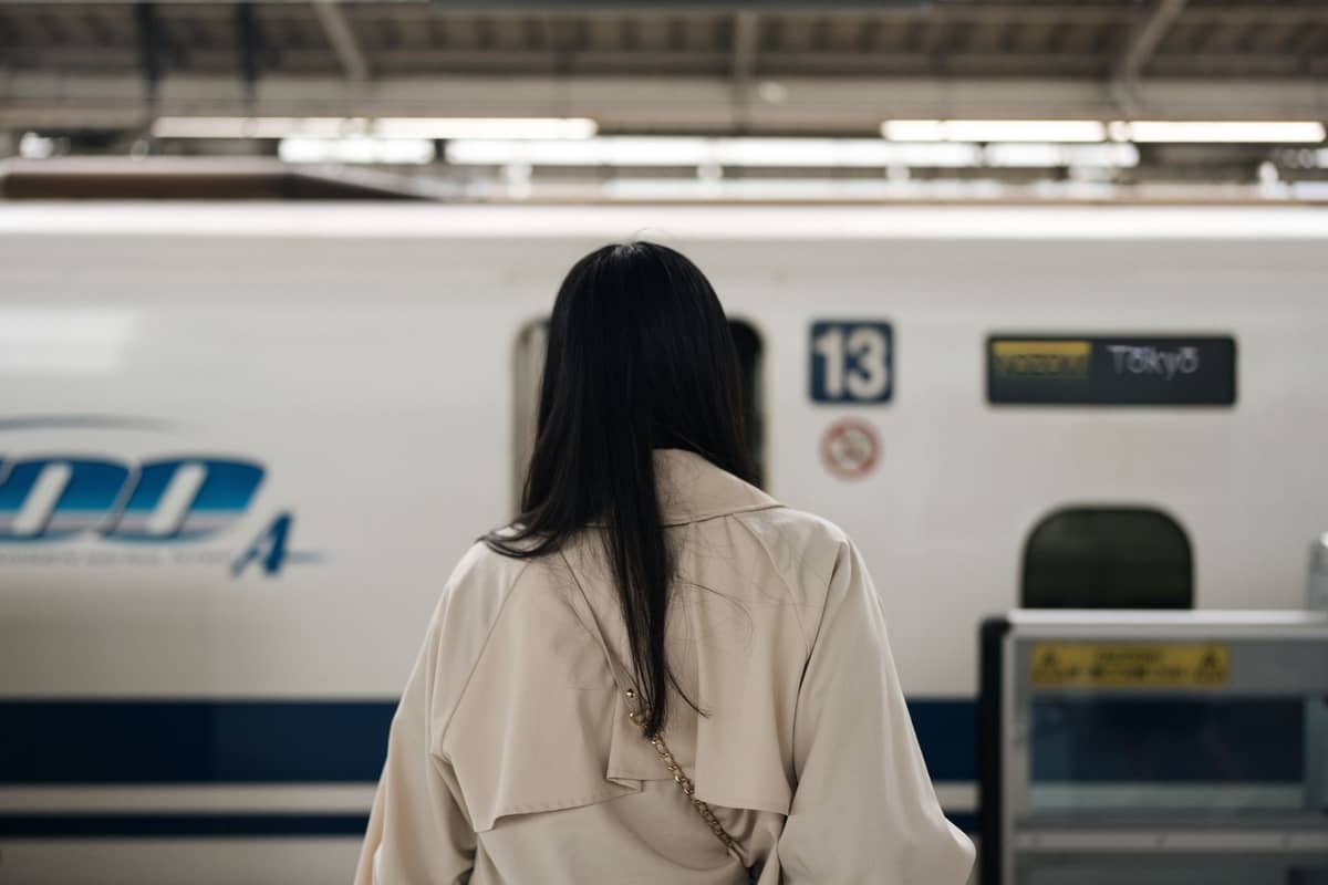 Person standing at a shinkansen platform in front of an N700A bullet train bound for Tokyo, inside a modern Japanese train station.