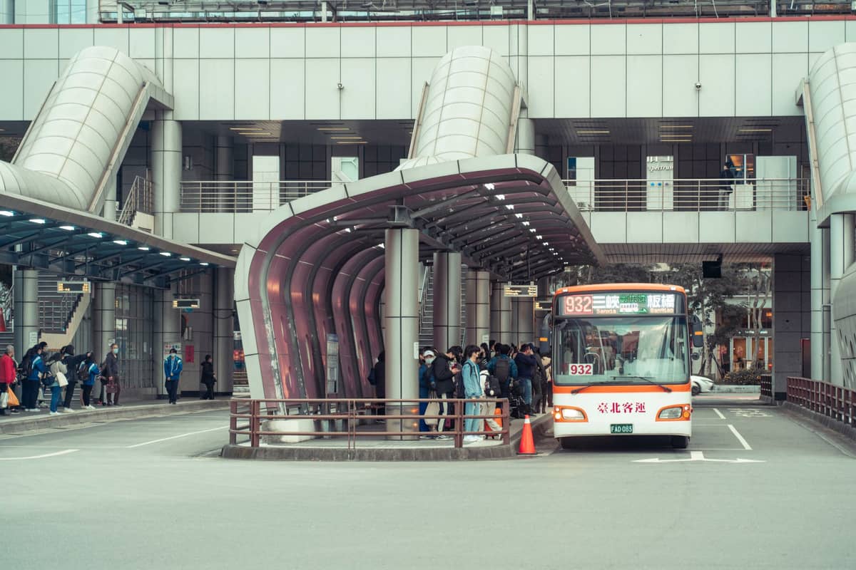 Wide view of a bus terminal in Japan with people boarding a bus under a modern canopy structure, daytime.
