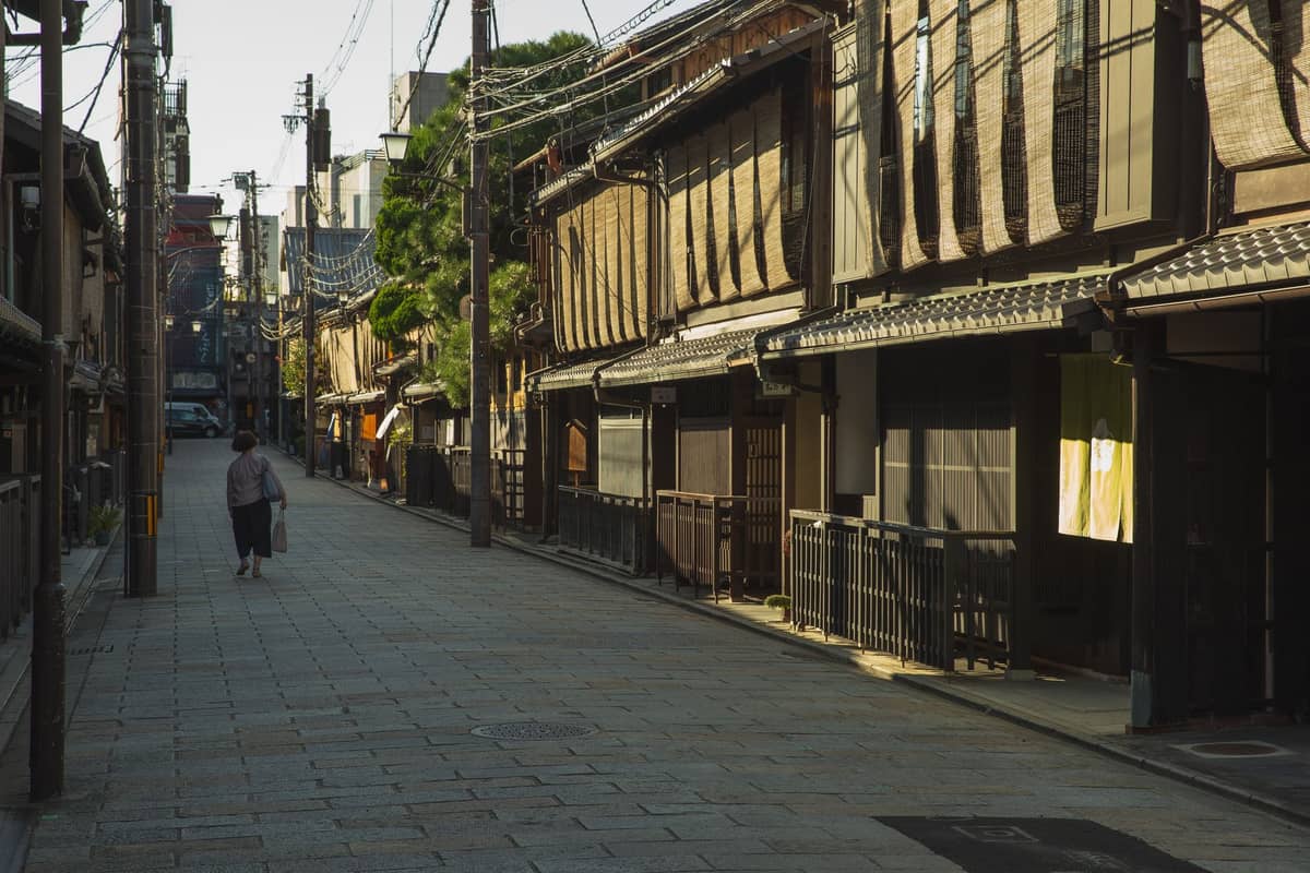 A quiet stone-paved street with traditional wooden buildings in Kyoto, early morning light and a lone person walking.