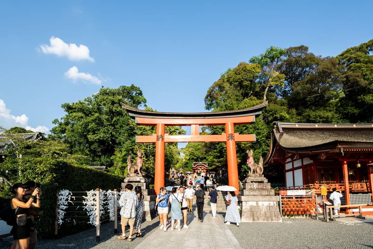 Wide view of Fushimi Inari-taisha’s main torii gate in Kyoto, with families and visitors walking under a sunny blue sky.