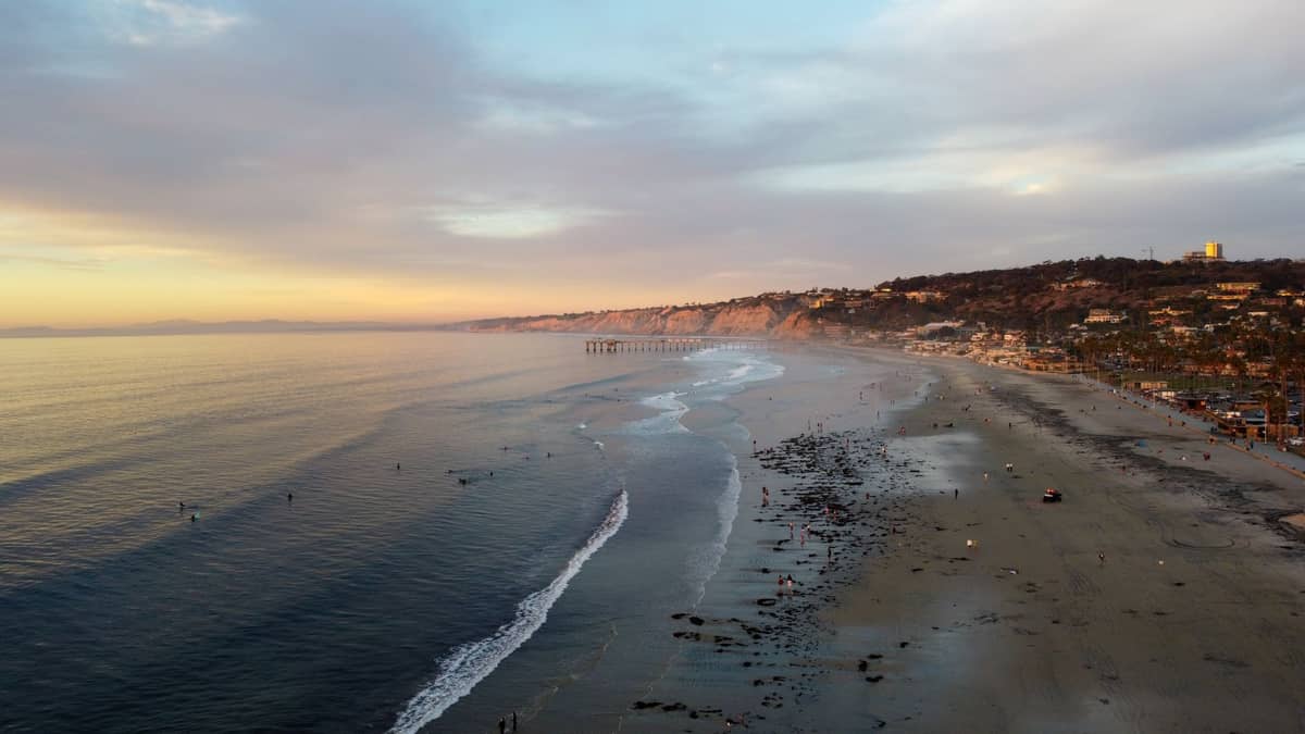 ภาพวิวพาโนรามาของชายหาด La Jolla Shores ยามเย็น เห็นริมหาดทราย คลื่นสงบ ท่าเรือไกล ๆ และหน้าผาล้อมรอบซานดิเอโก
