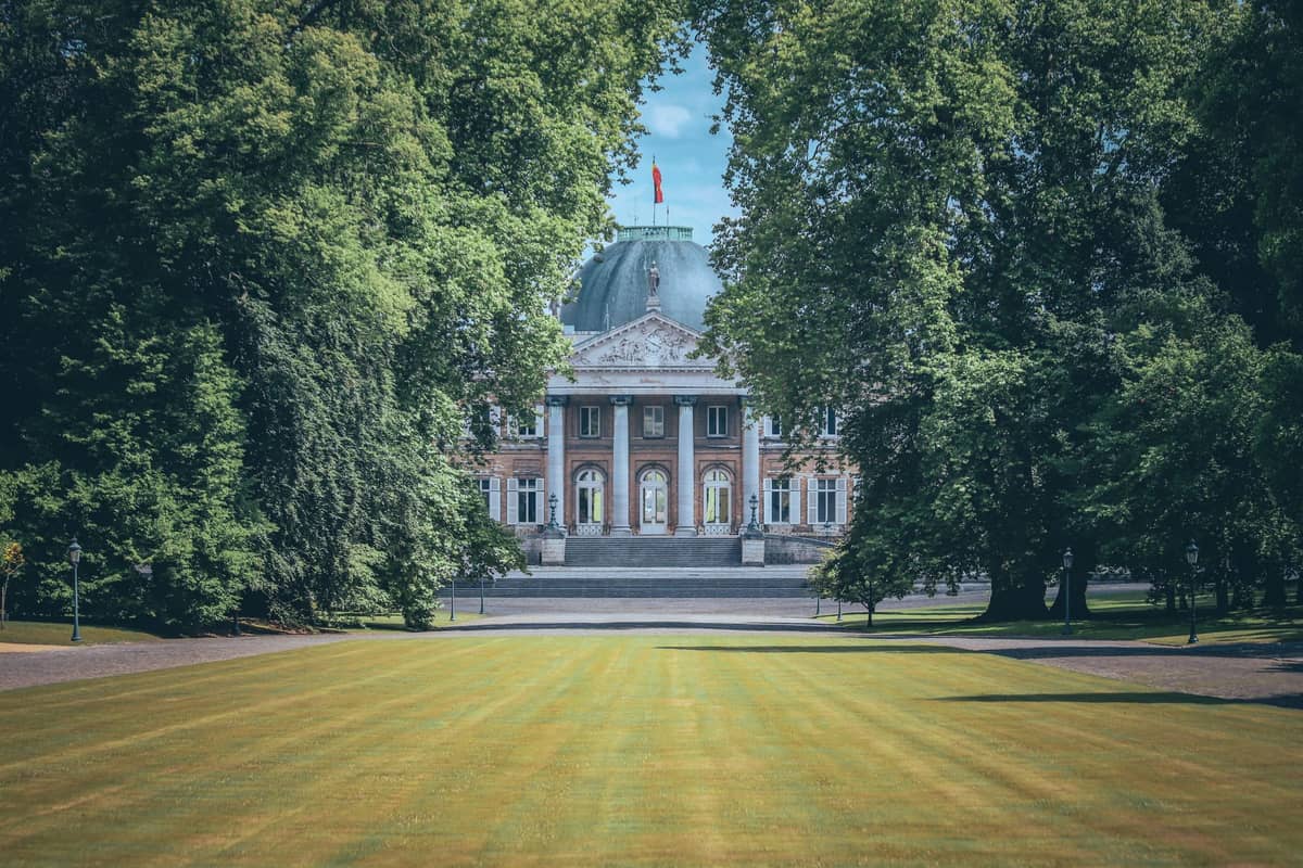 Castelo Real de Laeken emoldurado pelos gramados do parque cerimonial e altas árvores verdes no bairro de Laeken, em Bruxelas, num dia ensolarado.